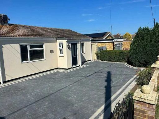 Bungalow with a paved driveway and well-kept hedges under a clear blue sky.