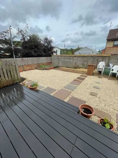 A gravel garden with stone pathways, potted plants, and wooden decking, under a cloudy sky.